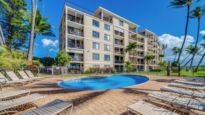 A hotel with a swimming pool, lounge chairs, and palm trees. - Kihei Beach #404- Serenity by the Shore (Kihei, Maui)