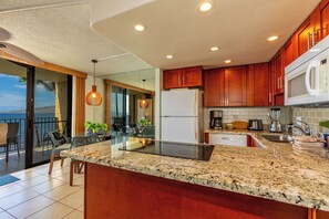 A modern kitchen with granite countertops, wooden cabinets, and a built-in microwave. - Kihei Beach #404- Serenity by the Shore (Kihei, Maui)