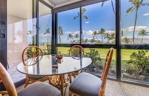 A glass table with chairs in a room with large windows overlooking palm trees and a grassy landscape.