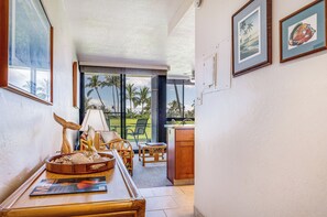 A room with a wooden dining table, a chair, a lamp, and a view of palm trees through a glass door.