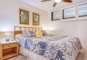 A bedroom with a bed, two bedside tables, a ceiling fan, and two windows with blinds.