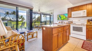 Une cuisine moderne avec des meubles en bois, une cuisinière blanche et une grande fenêtre donnant sur un paysage tropical.