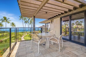 Un patio techado al aire libre con mesa y sillas, con vista panorámica al océano y palmeras.