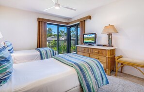 Habitación de hotel con dos camas, televisión, cómoda, lámpara y vistas a palmeras a través de amplias ventanas.