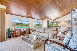 A spacious living room with a high ceiling, a large flat-screen TV, a comfortable sofa, a coffee table, and a lamp. - Oceanfront Gem with Mesmerizing Views and Lush Surroundings – Wailea Elua #1404 (Wailea, Maui)