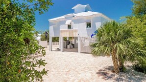 A white building with a flat roof, a covered entrance, and a paved area in front. - Coco Cay House on Coco Plum with pool and dock (Marathon)