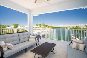 A balcony with a sofa, a table, and a view of a marina. - Coco Cay House on Coco Plum with pool and dock (Marathon)