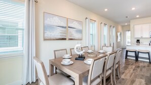 A dining area with a wooden table set for six, surrounded by chairs. There are three framed artworks on the wall above the table. - Relax & Reboot - Fantastic Margaritaville Cottage w/ Private Spa / Pool Combo (Kissimmee)