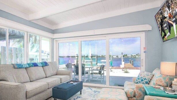 A living room with a sofa, ottoman, and patterned chairs, a coffee table, and a view of a marina through large sliding glass doors. - Sea La Vie 2 bedroom on open water in Kcb (Key Colony Beach)