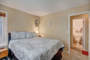 Une chambre à coucher comprenant un lit, une table de chevet, une lampe et une porte donnant sur une salle de bain.