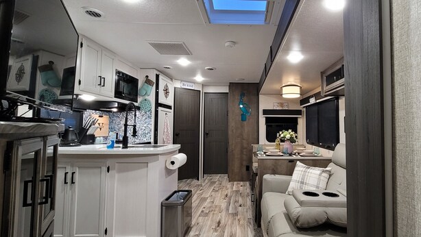 A compact RV kitchen with white cabinets, a microwave, and a sink. There is a small seating area with a cushion and a window above it. - Hidden gem in Key Largo, bunk room, outdoor kitchen, 2 pools, laundry, 2 beaches (Key Largo)