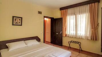 A hotel room with a large bed, a bedside table, a small chair, a window with curtains, and a door.