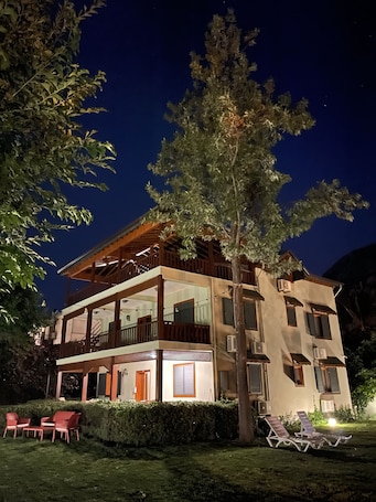 A two-story building with a balcony, outdoor seating, and a tree in front.
