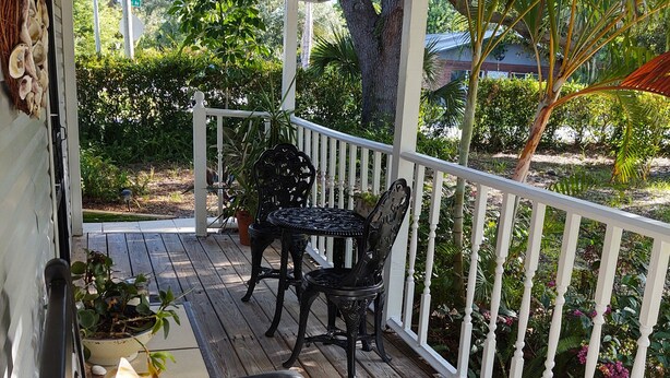 A covered outdoor area with a wooden deck, white railing, and a table with chairs. - Great location.  Ten minutes from  Beach.  Peaceful retreat! (Merritt Island)
