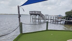 A grassy area with a wooden dock extending into a body of water, a blue canopy, and a small structure on the dock. - Great location.  Ten minutes from  Beach.  Peaceful retreat! (Merritt Island)