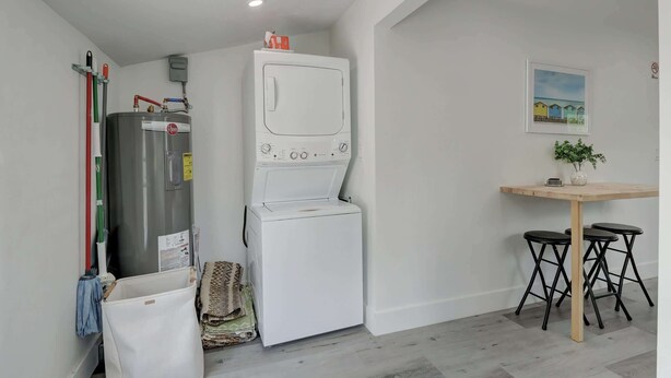 Een kleine keuken met een witte koelkast, een spoelbakje en een eethoek met een tafel en twee krukken.