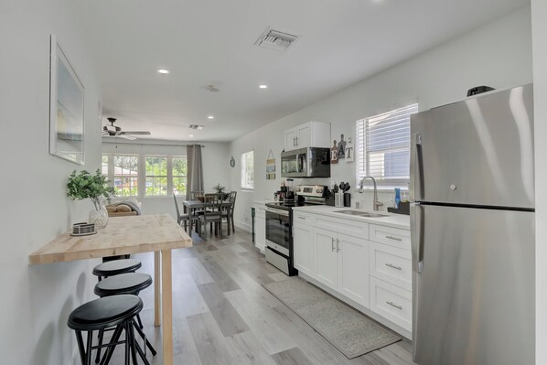 A modern kitchen with white cabinetry, a stainless steel refrigerator, and a dining area with a wooden table and bar stools.