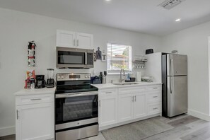 A modern kitchen with white cabinetry, a stainless steel refrigerator, a built-in oven, a microwave, and a coffee maker.