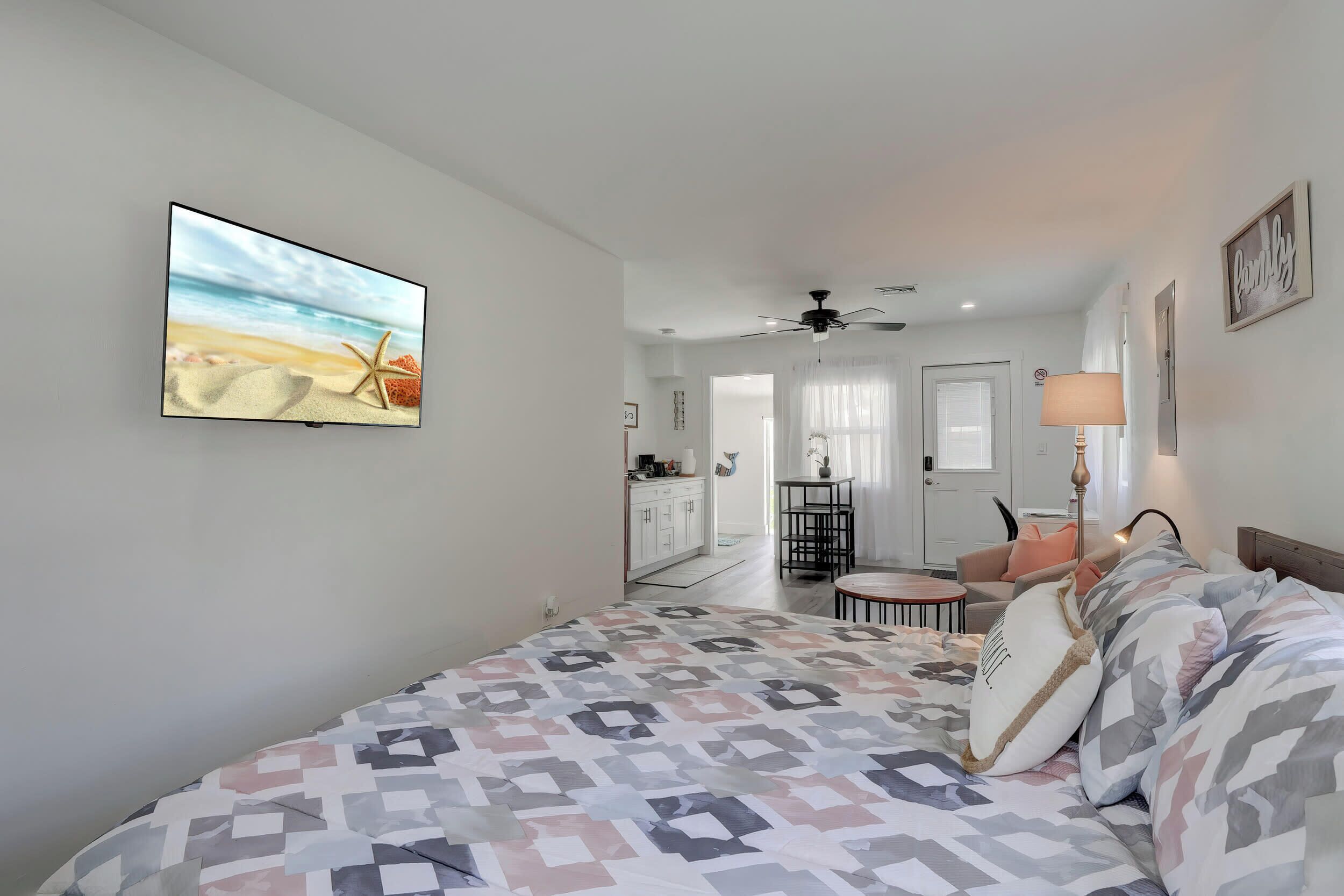 Una camera da letto con un letto, una TV, una ventola a soffitto e vista sull'area living.
