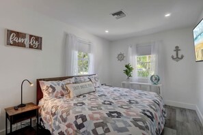 A bedroom with a bed, a nightstand, a wall-mounted fan, and a window with curtains.