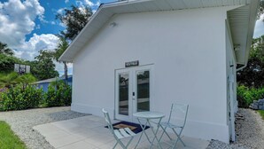 A small white building with a door and windows, a small patio with a table and chairs, and a sign above the door.