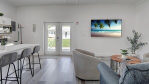 Una sala de estar moderna con un ventanal grande, un comedor con taburetes de bar y un cuadro de una playa.