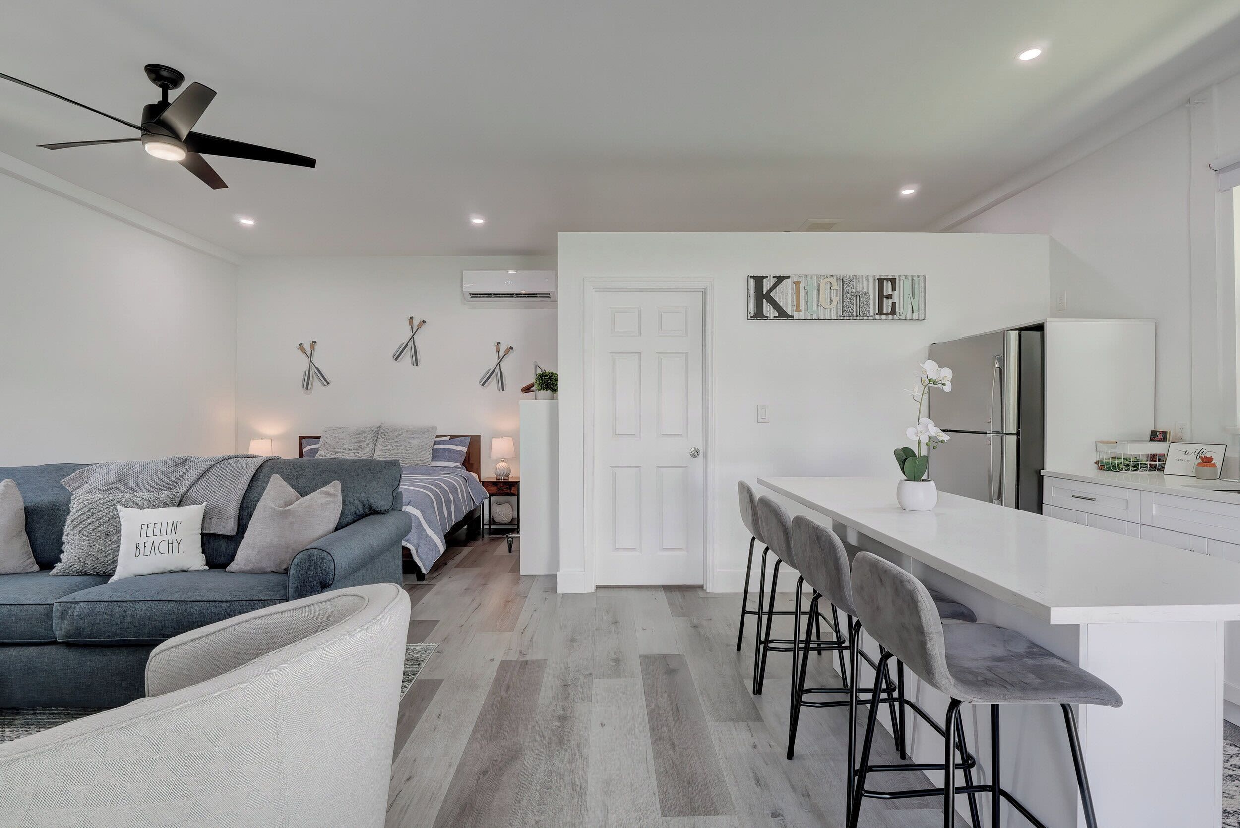 A modern kitchen with a white countertop, bar stools, and a refrigerator.
