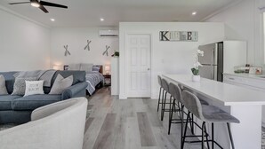 A modern kitchen with a white countertop, bar stools, and a refrigerator.
