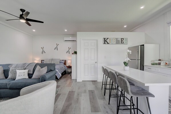 A modern kitchen with a white countertop, bar stools, and a refrigerator.