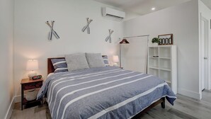 Un dormitorio con cama, lámparas de noche, aire acondicionado de pared y un armario.