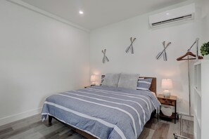 A bedroom with a bed, bedside tables, a hanging plant, and an air conditioning unit.