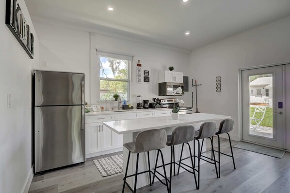 A modern kitchen with a large island, stainless steel appliances, and a view to the outside.