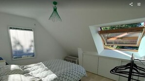 Un dormitorio con cama, ventana con vistas, lámpara colgante y radiador.