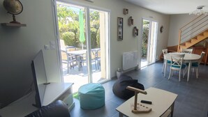 Amplia sala de estar con un gran ventanal corredero que da a un patio, una mesa de comedor con sillas, un sofá y una escalera.
