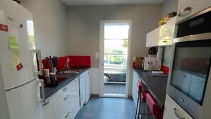 Cocina compacta con armarios blancos, encimera roja, ventilador de techo y vistas al exterior.