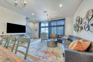 Amplia sala de estar con una televisión de pantalla plana grande, un sofá de cuero, una mesa de centro y una escalera que conduce a un piso superior.