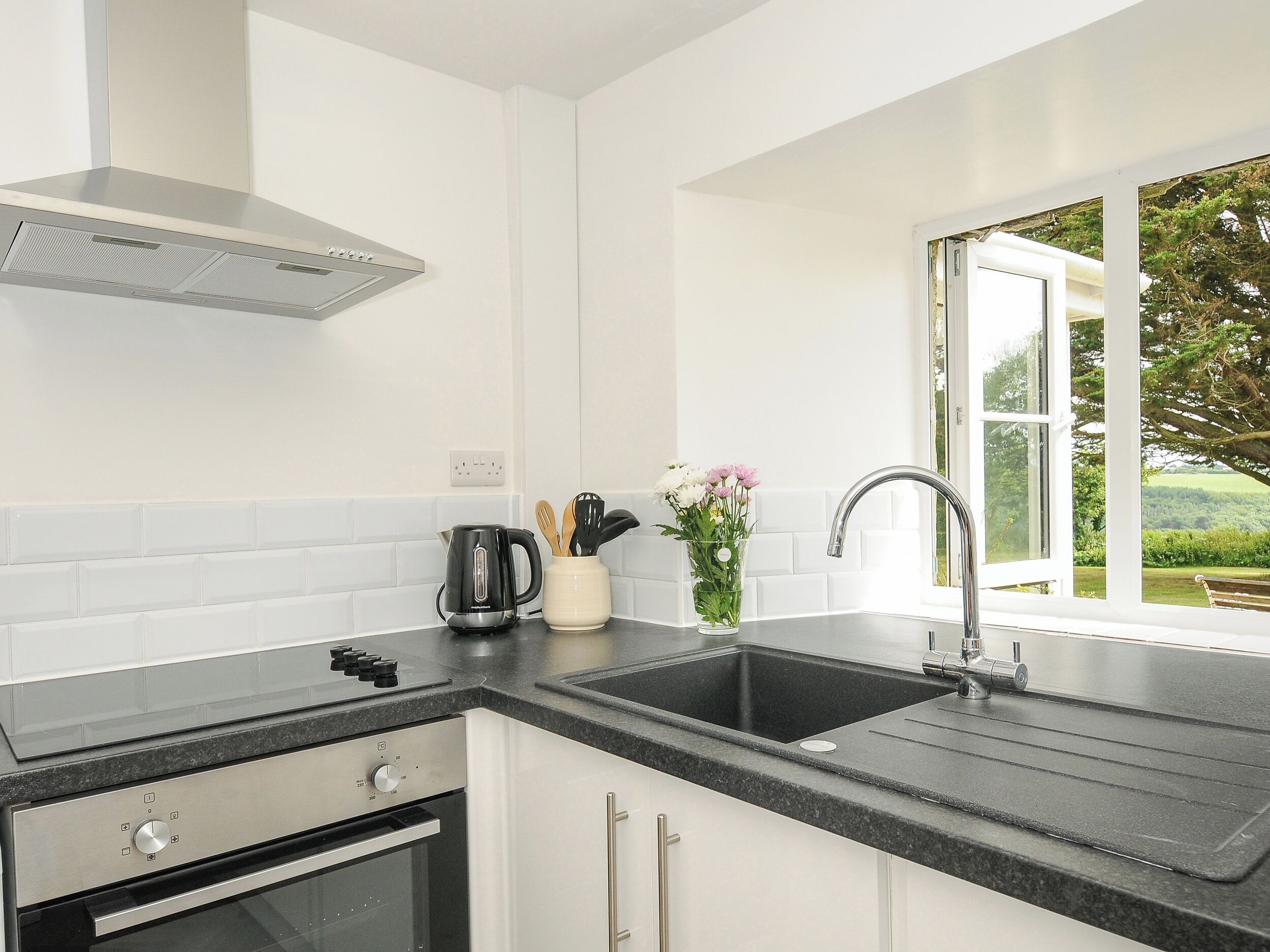 A modern kitchen with a black countertop, stainless steel appliances, a window with a view of greenery, and a white backsplash.