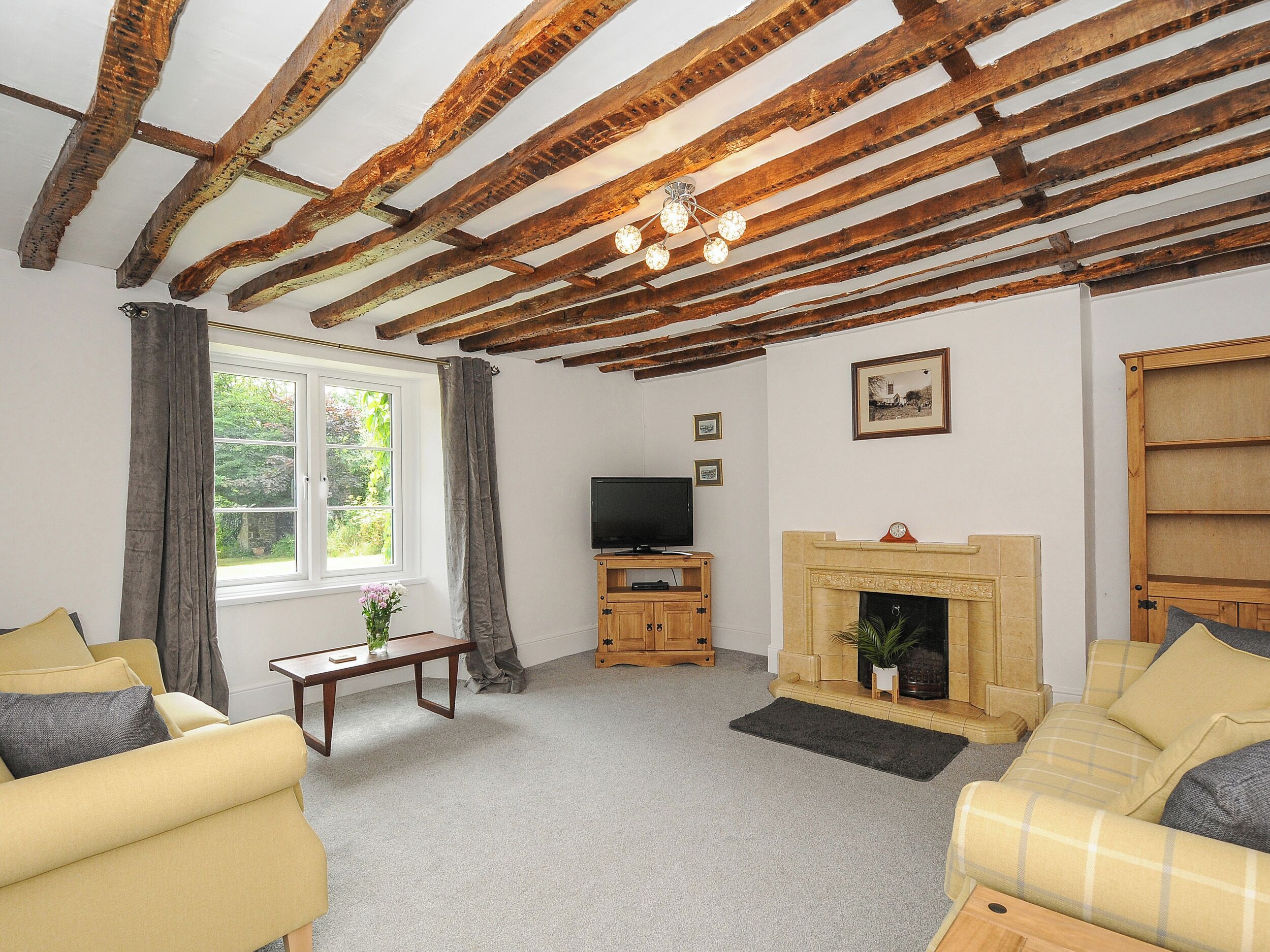A living room with exposed wooden beams, a fireplace, a television, and two sofas.
