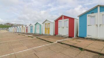 A row of colorful beach huts with white doors and windows, numbered sequentially, on a paved beach area.