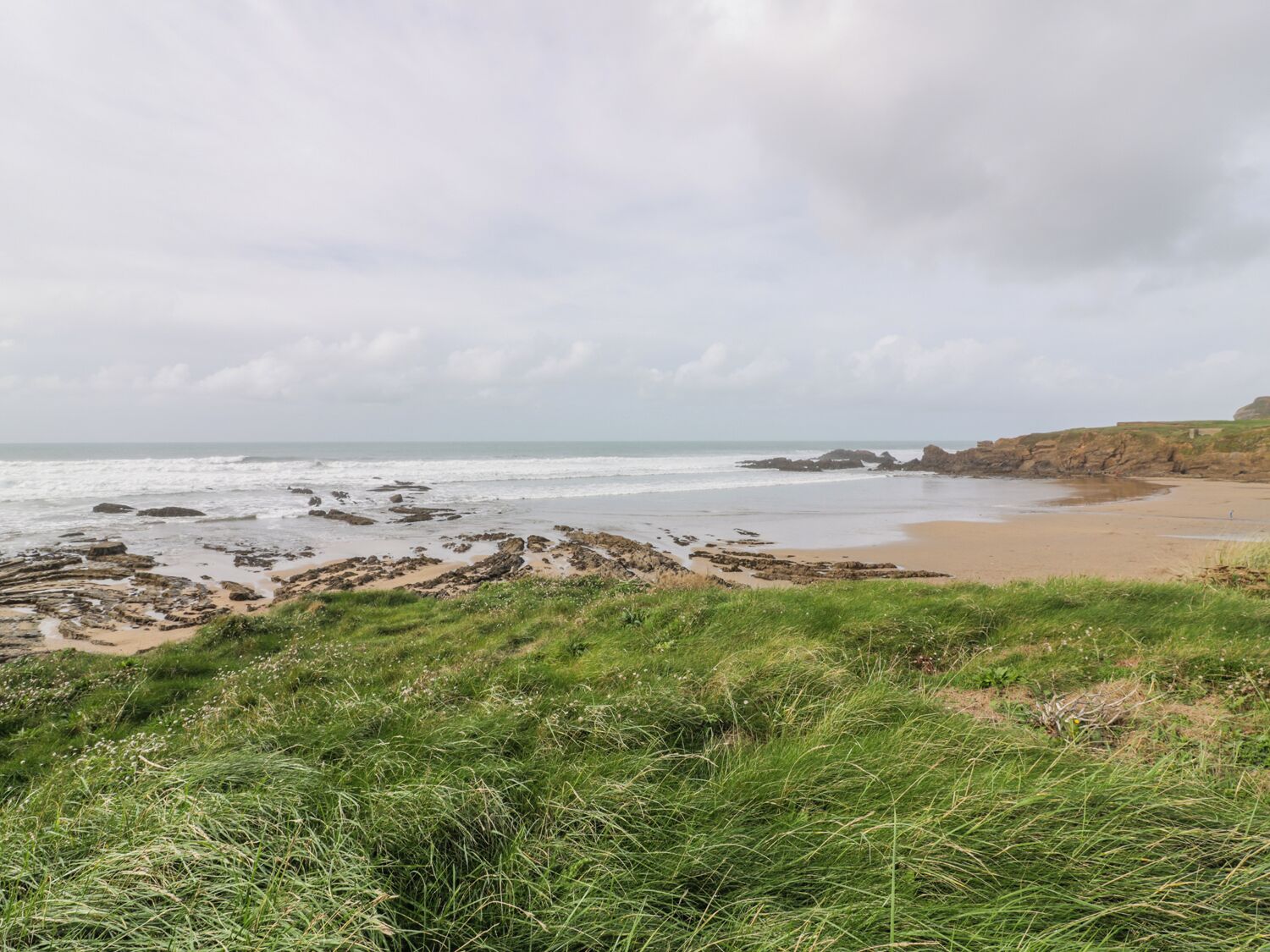 Un paisaje costero con playa arenosa, afloramientos rocosos y terreno cubierto de hierba.