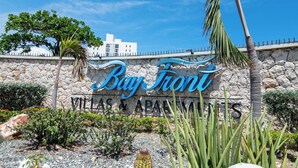 A sign for 'Bay Front Villas & Apartments' with a stone wall and palm trees. - Gated Beachfront House - 10 Minutes from Kingston (Portmore)