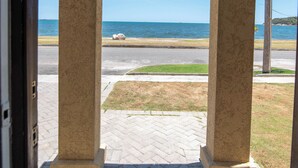 An outdoor view through a wooden pergola with a stone pillar, overlooking a paved area and a body of water. - Gated Beachfront House - 10 Minutes from Kingston (Portmore)