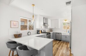A modern kitchen with white cabinetry, a central island, bar stools, and pendant lighting.