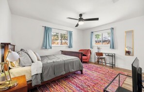 A bedroom with a bed, desk, chair, TV, and a ceiling fan.