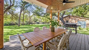 A wooden deck with a table and chairs, a ceiling fan, and a grill. - The Creek Villa | Concierge Services (Horseshoe Bay)