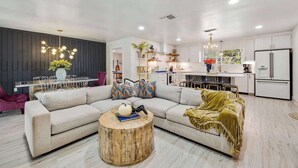 A modern living room with a sectional sofa, a round coffee table, and a dining area with a glass table. - The Creek Villa | Concierge Services (Horseshoe Bay)
