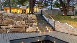 A stone staircase leading to a modern house with a wooden deck and outdoor lighting. - The Creek Villa | Concierge Services (Horseshoe Bay)