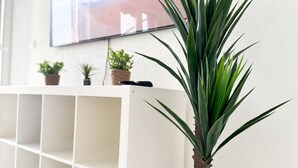 Une plante en pot, placée dans un pot à texture particulière, une étagère blanche et, au mur, un tableau représentant une scène de plage.