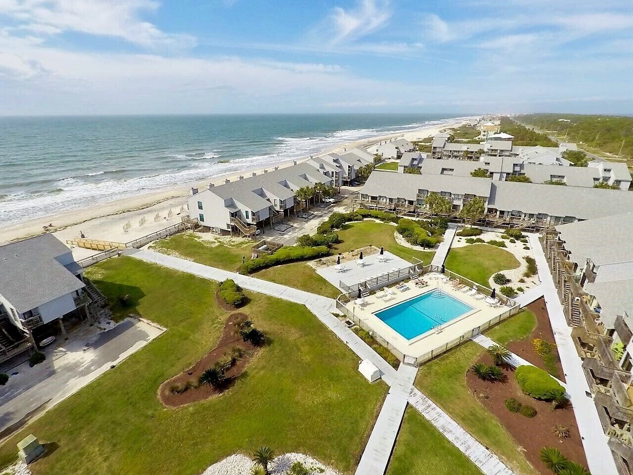 An aerial view of a coastal resort with a swimming pool, beachfront, and multiple buildings.