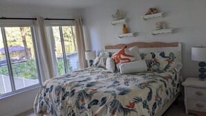 Ein Schlafzimmer mit Bett, Nachttisch, Lampe, einem Fenster mit Vorhängen und Seeblick.